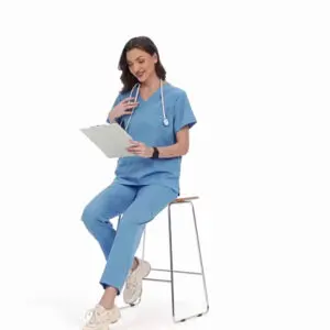 Female healthcare worker in blue scrubs sitting on a stool with a clipboard.